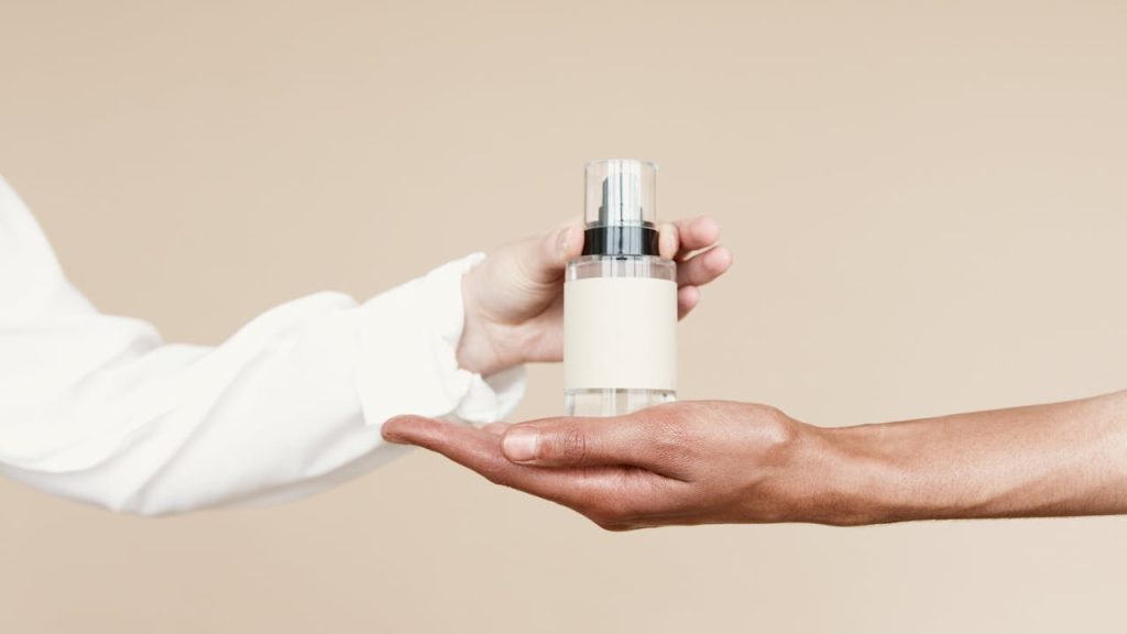 Minimalist shot of a perfume bottle being passed between hands against a neutral background.
